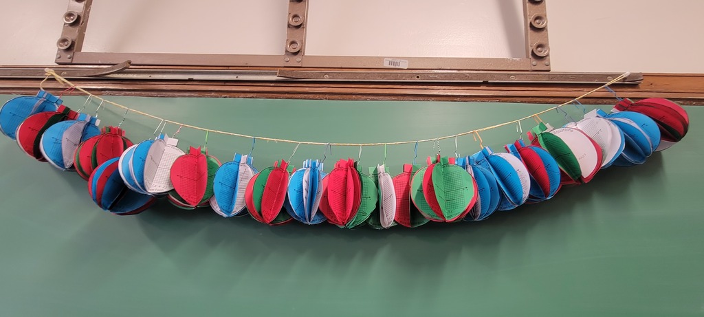 Blue, white, green and red ornaments strung together over a green chalk board.