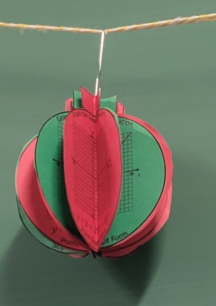 Red and green ornament with graphs in the folds hung in front of a green chalkboard.